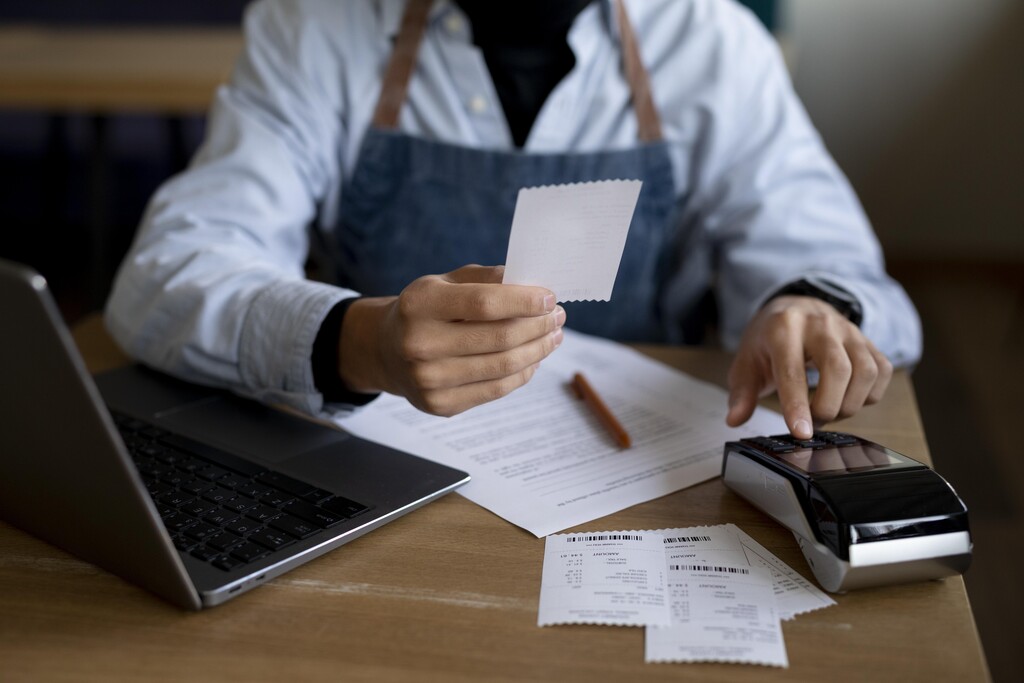 homem com papeis na mão usando calculadora ao lado de notebook